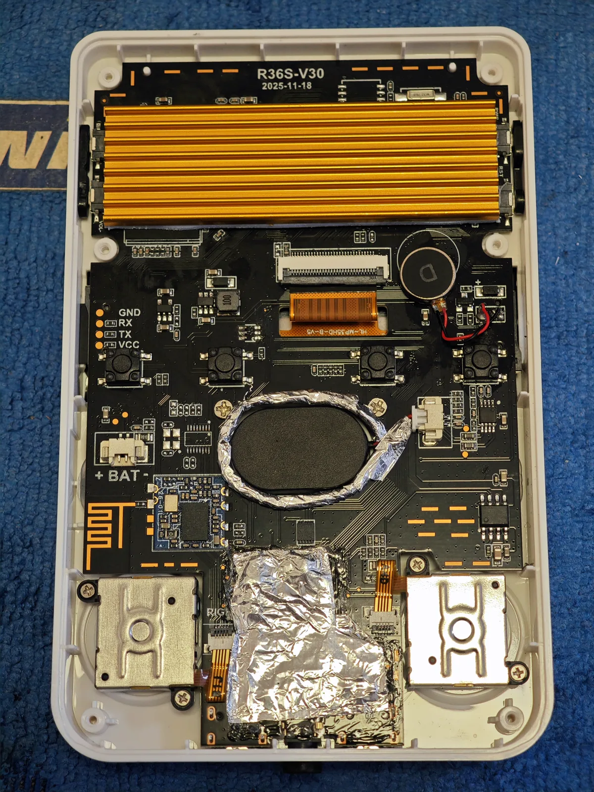 Foil tape, added by hand. Not a stock part. The owner wrapped the round speaker in aluminum tape and laid a second patch over the board below it. It is on this page because it is what was actually done to this unit, not because it is fitted to the units we send: the WiFi builds are the ones with the faint speaker hum our product page discloses, and this was one owner's attempt at it. Nothing here is measured and we make no claim that it worked.