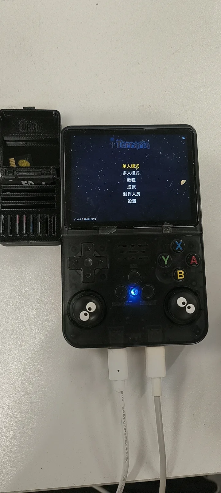 A black R36S held in two hands on the title screen of a game its owner installed, with a cable connected